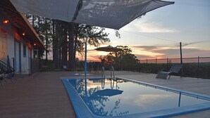 Piscina al aire libre con borde azul, rodeada de sillones de descanso y una zona de estar cubierta.