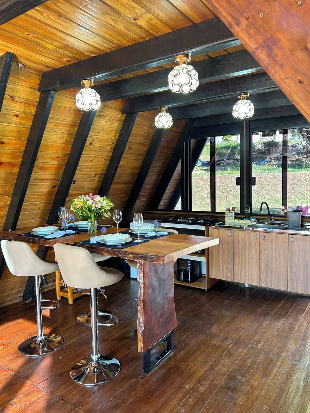 Un comedor con una mesa de madera, taburetes de bar y una cocina al fondo.