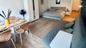 Ett kompakt bostadsutrymme med en säng, en soffa, ett litet bord och en matplats med stolar.