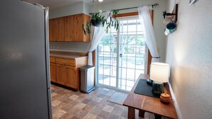 A kitchen with wooden cabinets, a refrigerator, a sink, and a window with curtains. - 4-Bedroom Home with Fenced Backyard (Lander)