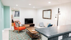 A modern living room with a sofa, a wooden coffee table, a TV, and a kitchen counter. - 4-Bedroom Home with Fenced Backyard (Lander)
