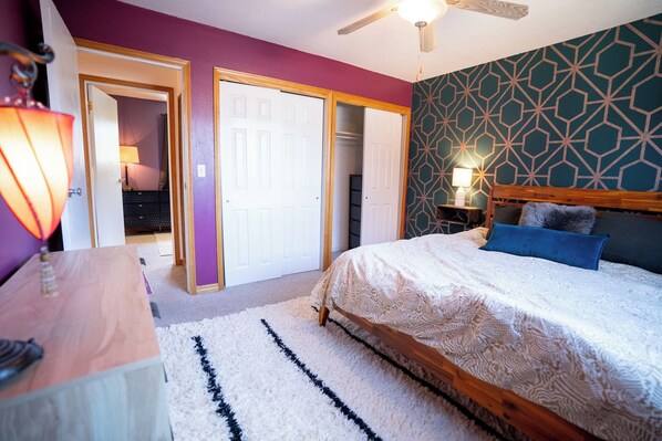A bedroom with a bed, a wooden dresser, a ceiling fan, and a patterned wall. - 4-Bedroom Home with Fenced Backyard (Lander)