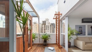 Un balcon avec un plancher en bois, des plantes en pot, un tapis de yoga et un canapé.