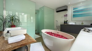 Une salle de bain moderne avec une baignoire sur pieds remplie de pétales de roses, un lavabo avec des articles de toilette et un grand miroir.