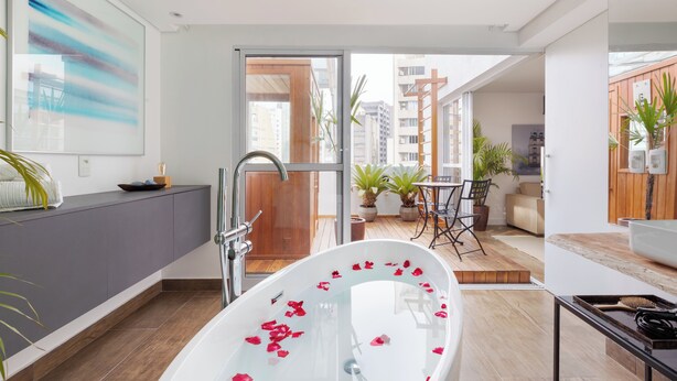 Une salle de bain moderne avec une baignoire sur pieds, une douche et un lavabo. Un balcon agrémenté de plantes en pot et d’un coin salon est également prévu.