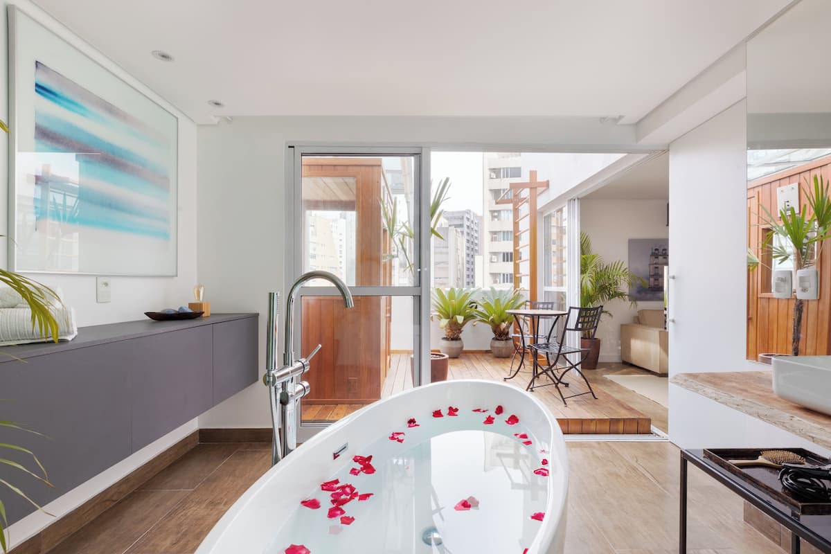 Ein modernes Badezimmer mit einer freistehenden Badewanne, einer Dusche und einem Waschbecken. Ein Balkon mit Blumentöpfen und einer Sitzecke ist ebenfalls vorhanden.