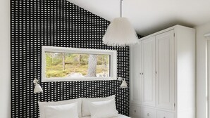 A bedroom with a bed, a window with a view of trees, a white wardrobe, and a white lamp.