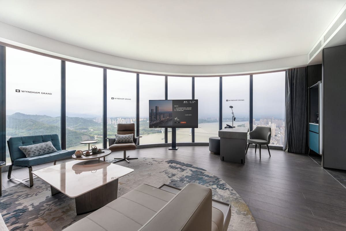 Una sala de estar moderna con un televisor grande, asientos cómodos y vistas de la ciudad a través de amplias ventanas.