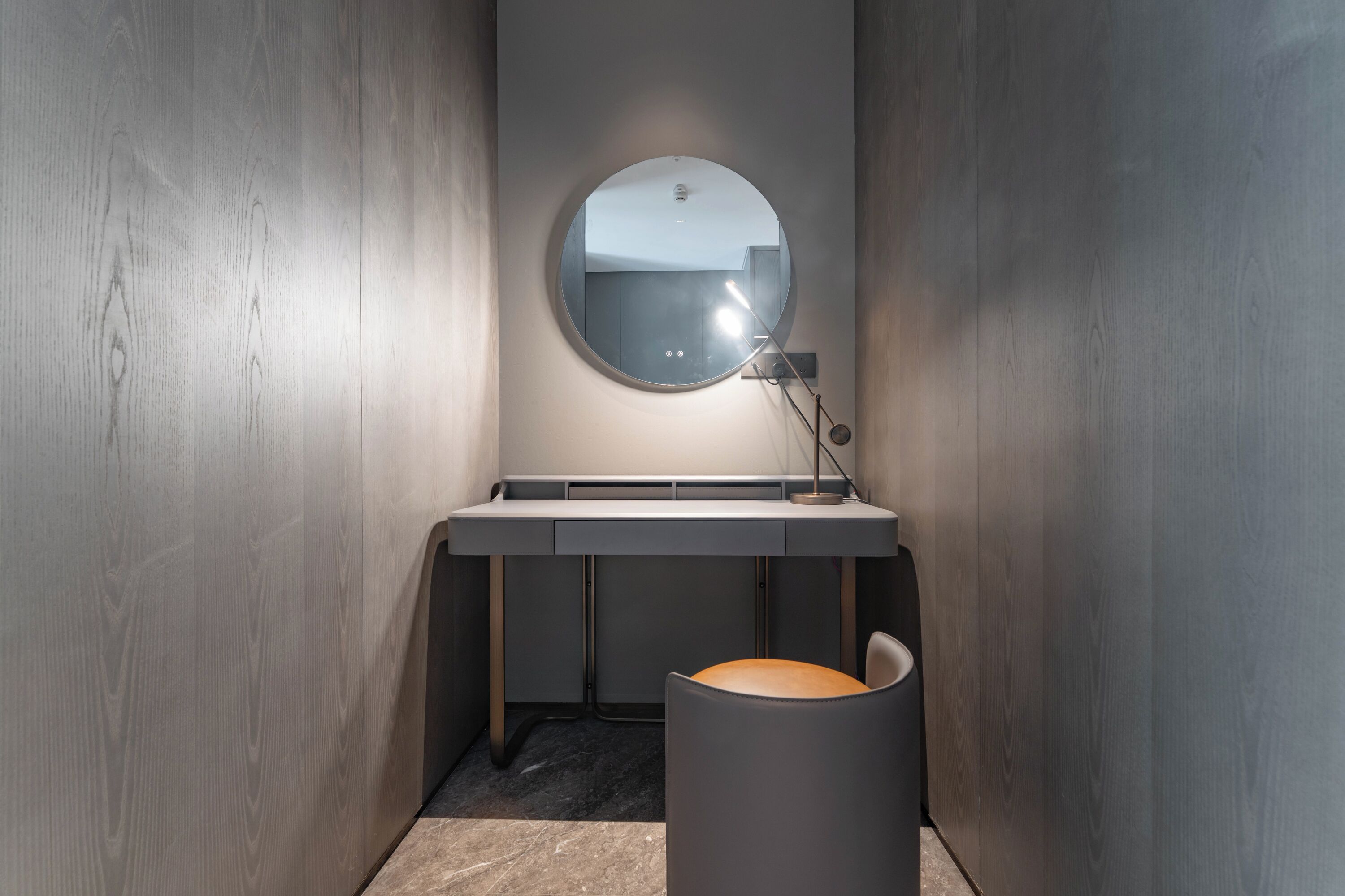 A modern bathroom with a round mirror, a small sink, and a chair.