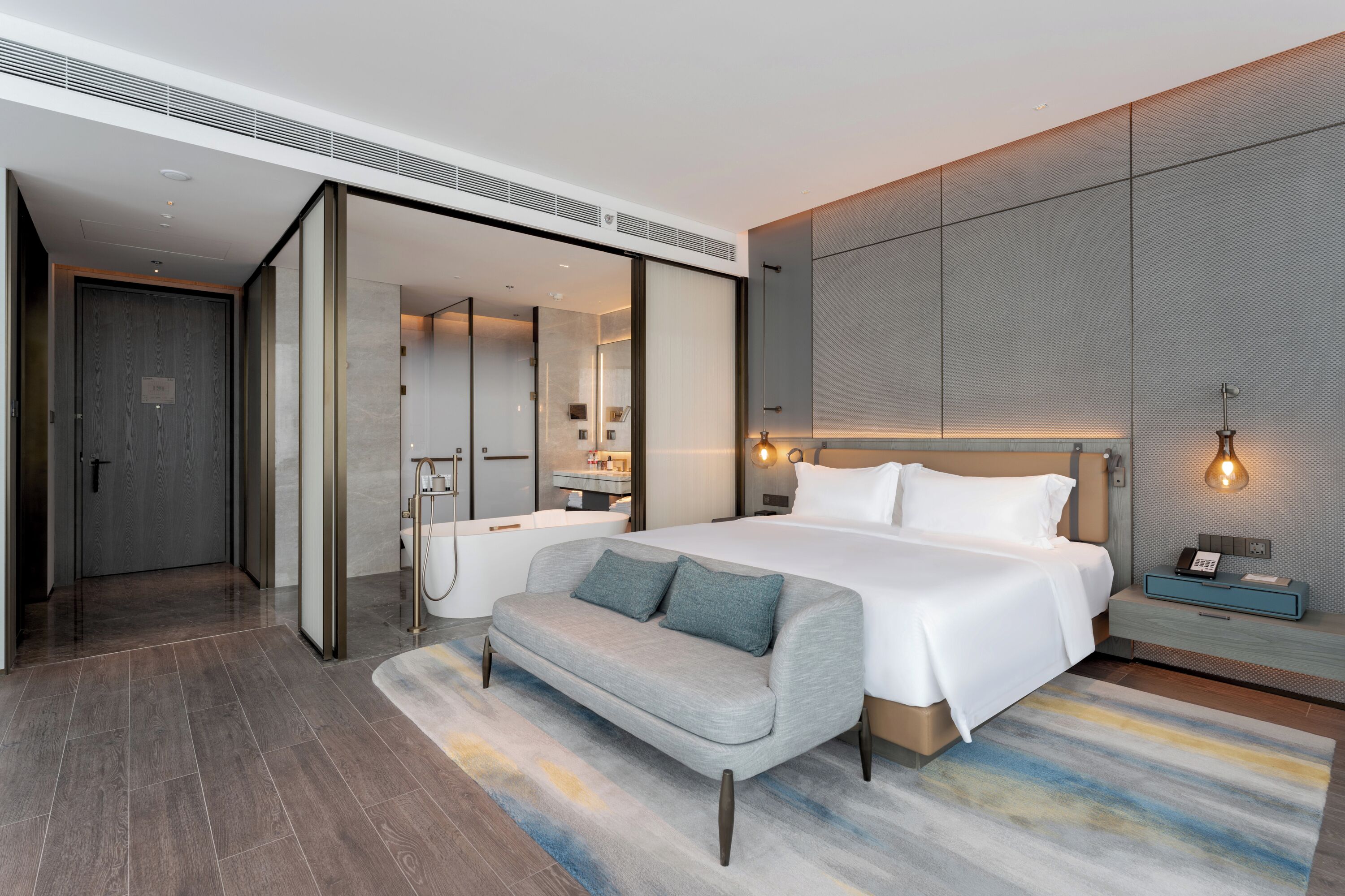 Una habitación de hotel moderna con una cama grande, un sofá, un baño y un vestidor.