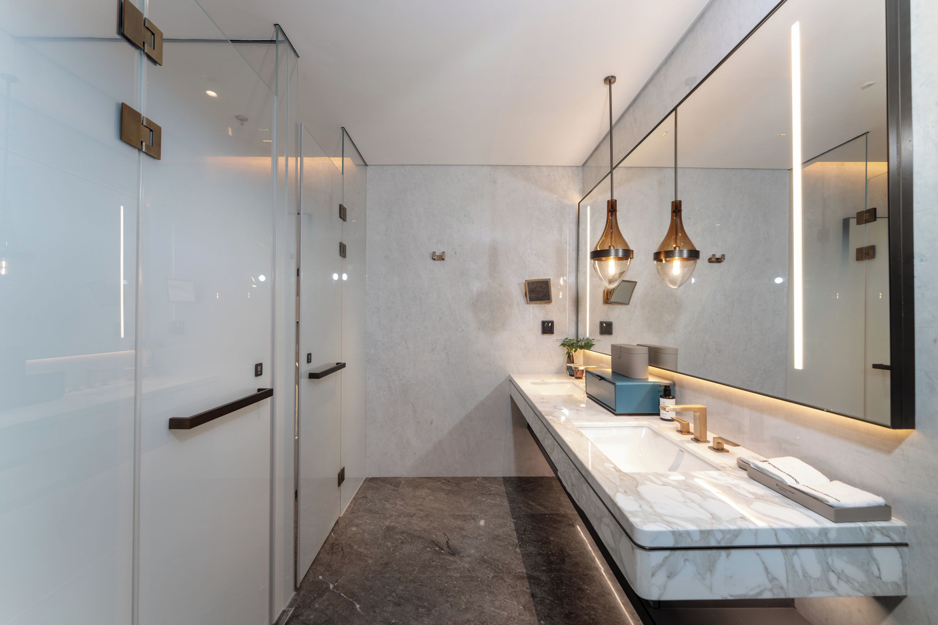 A modern bathroom with a marble sink, glass shower enclosure, and pendant lighting.