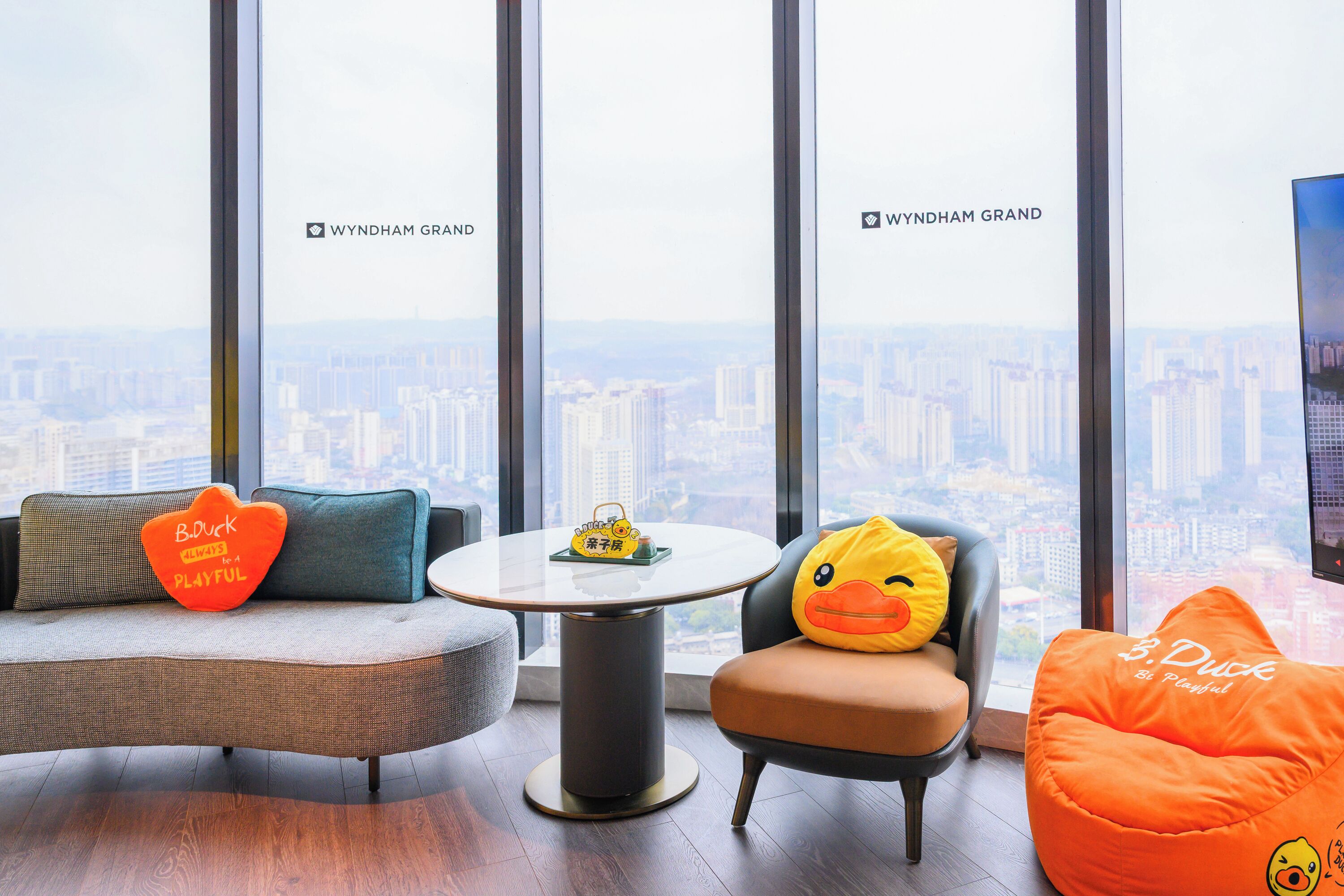 A modern interior with a sofa, a chair, a small table, and a large window with a city view.