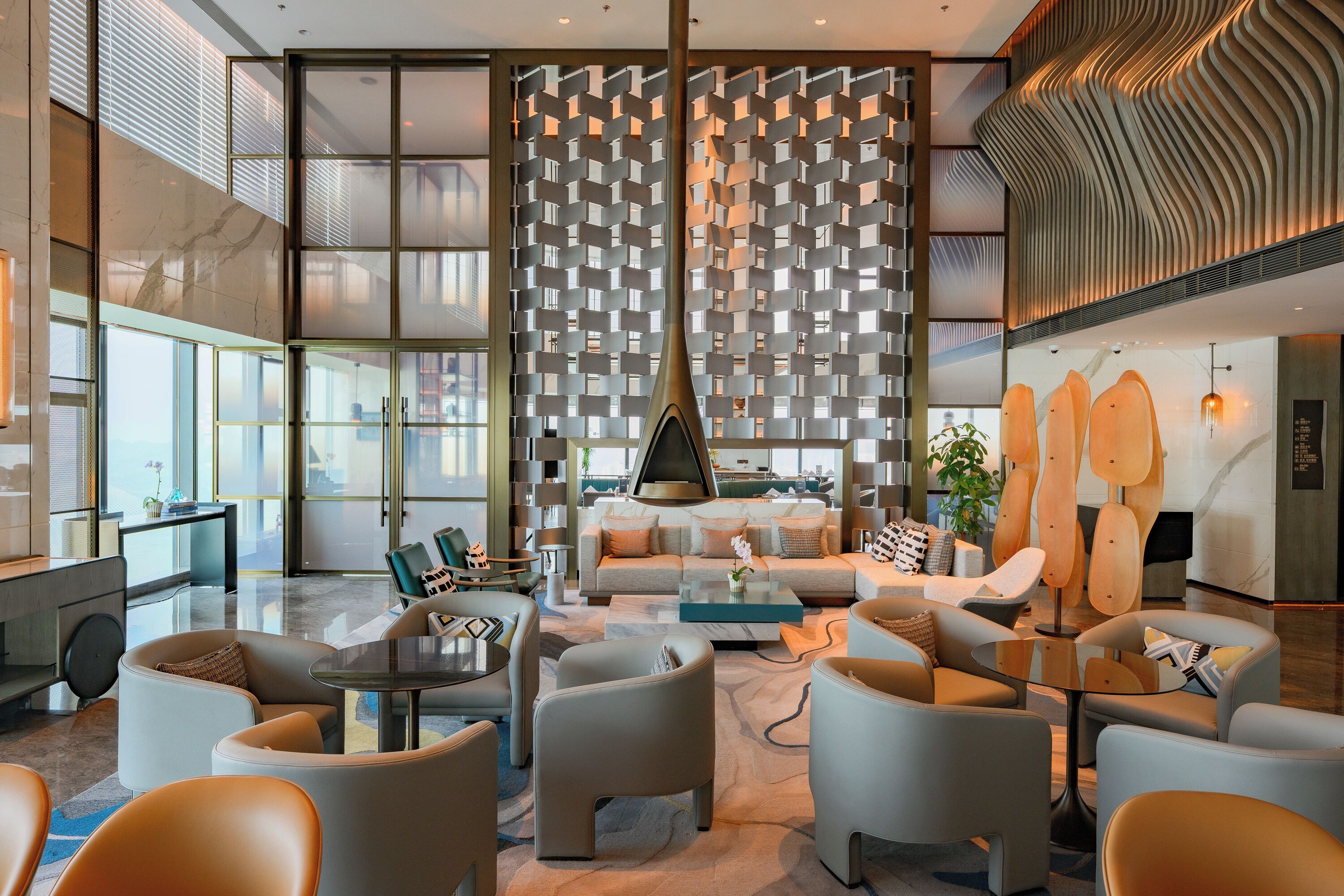 Un hall d’hôtel moderne doté d’un espace salon central, d’une grande paroi vitrée et d’un design de plafond original.