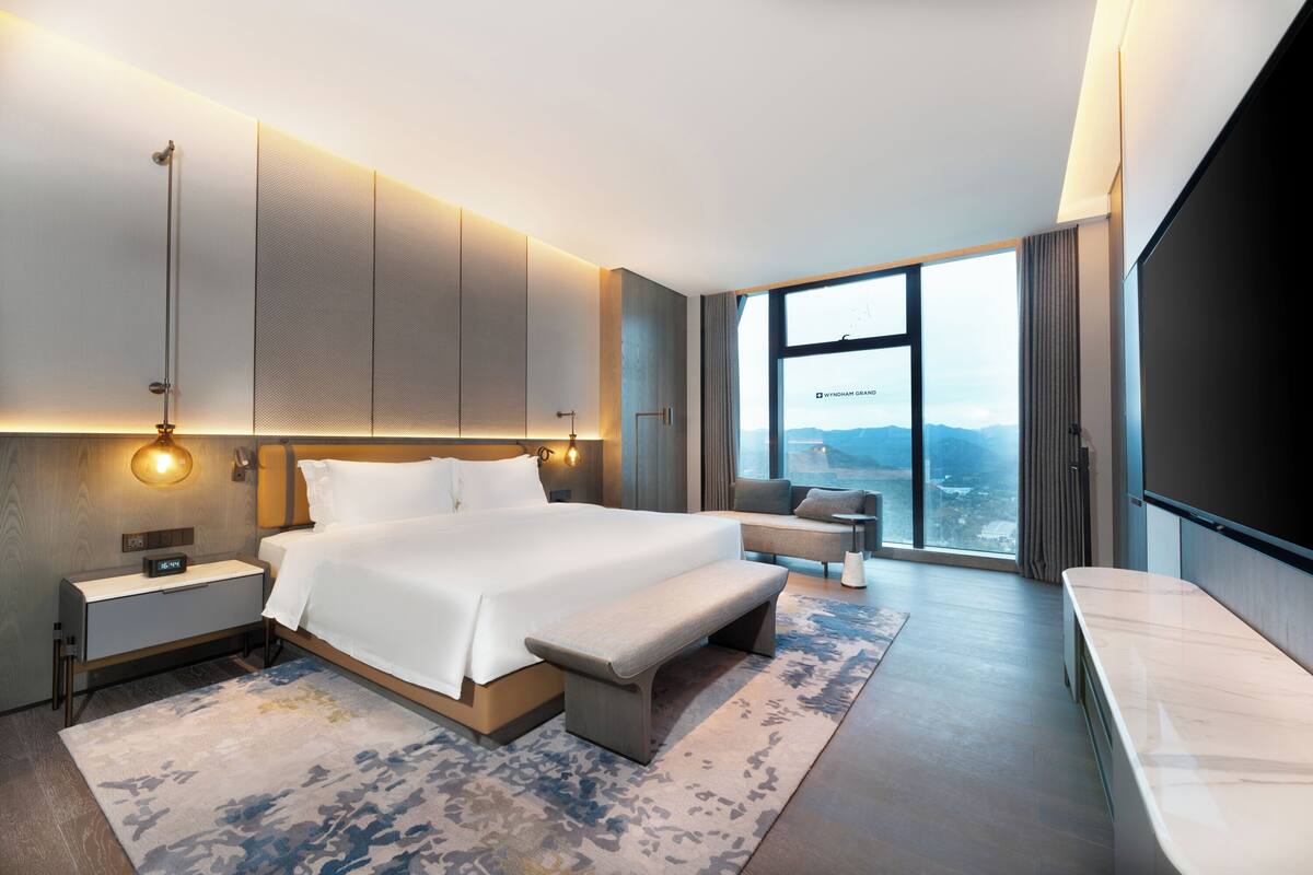 Una habitación de hotel moderna con una cama grande, un banco, un escritorio y un televisor.