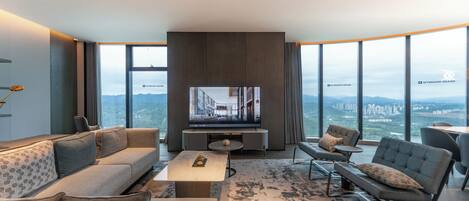 Una sala moderna con un televisor de pantalla plana grande, un sofá, una mesa de centro y vistas a un paisaje urbano a través de amplios ventanales.
