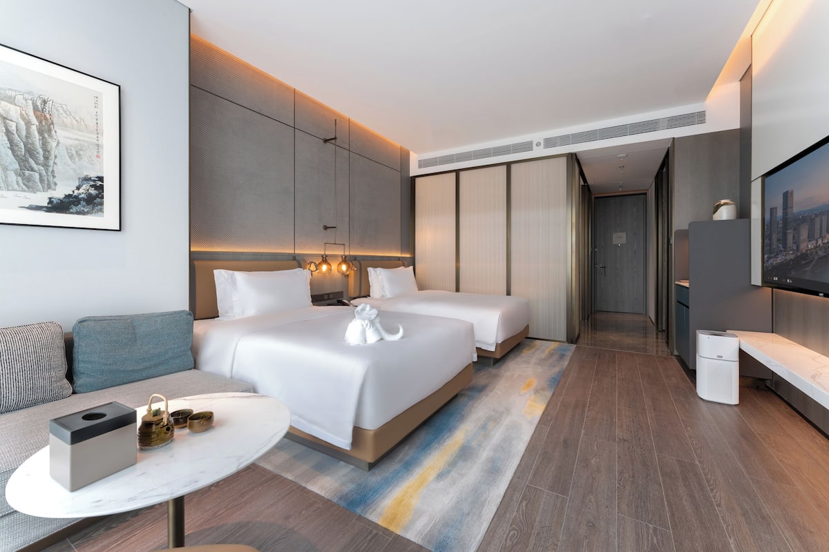 Una habitación de hotel moderna con una cama grande, un sofá, una mesita y un televisor.