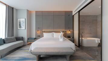 Una habitación de hotel moderna con una cama grande, un banco, un sofá, una bañera y un televisor montado en la pared.