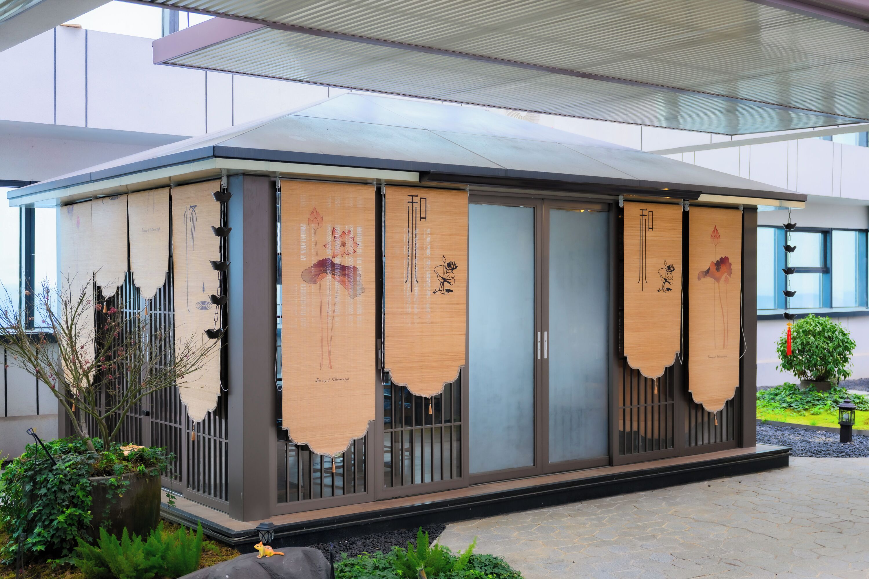 A modern building with large glass doors, a covered entrance, and a garden area with plants and a small tree.