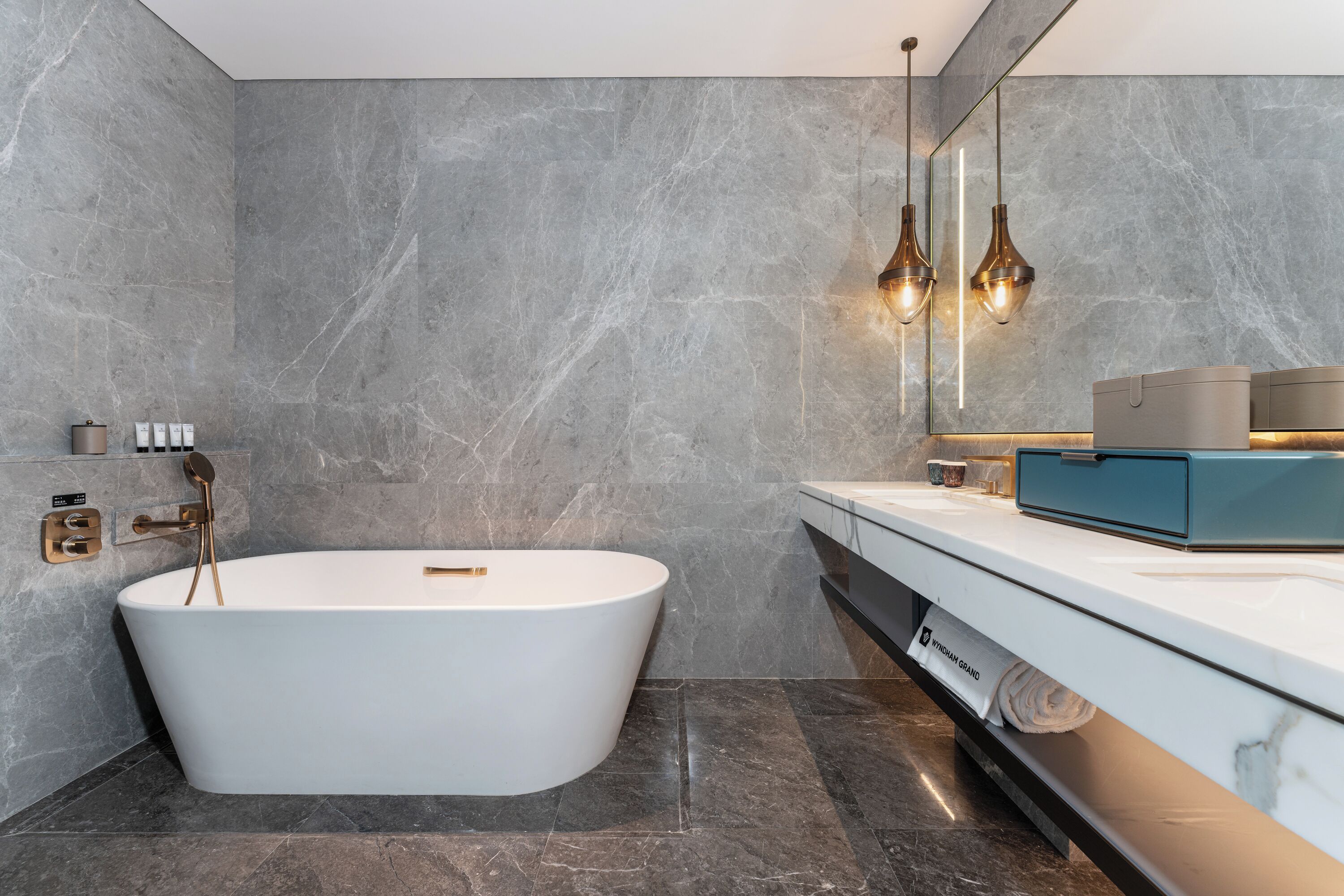 Un baño moderno con una bañera independiente, paredes de mármol y un mueble de tocador con dispensador de toallas.