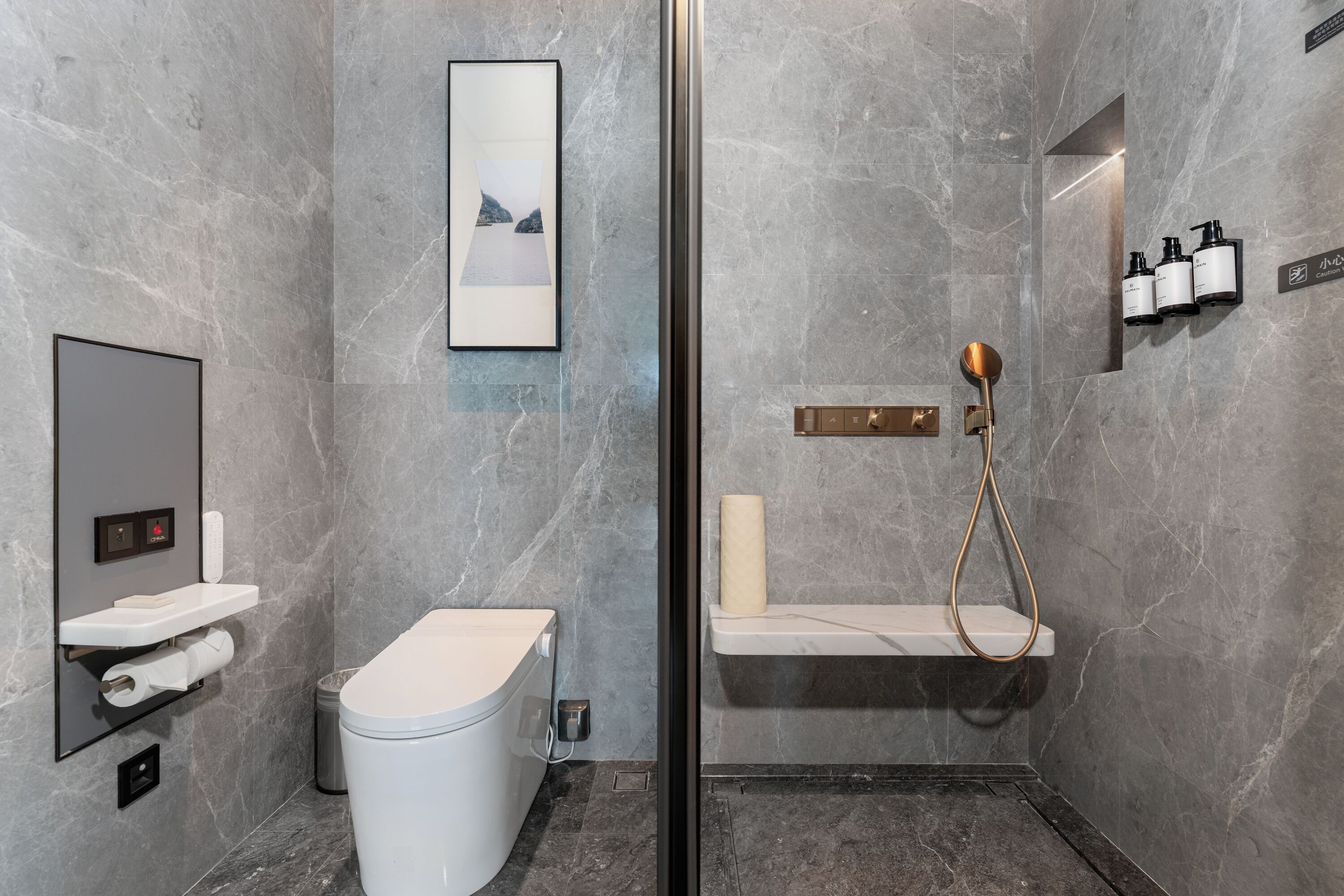 A modern bathroom with a toilet, sink, and shower area, marble walls, and a framed picture.