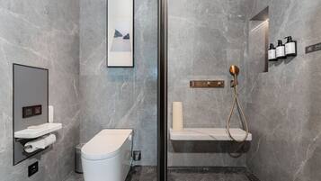A modern bathroom with a toilet, sink, and shower area, marble walls, and a framed picture.