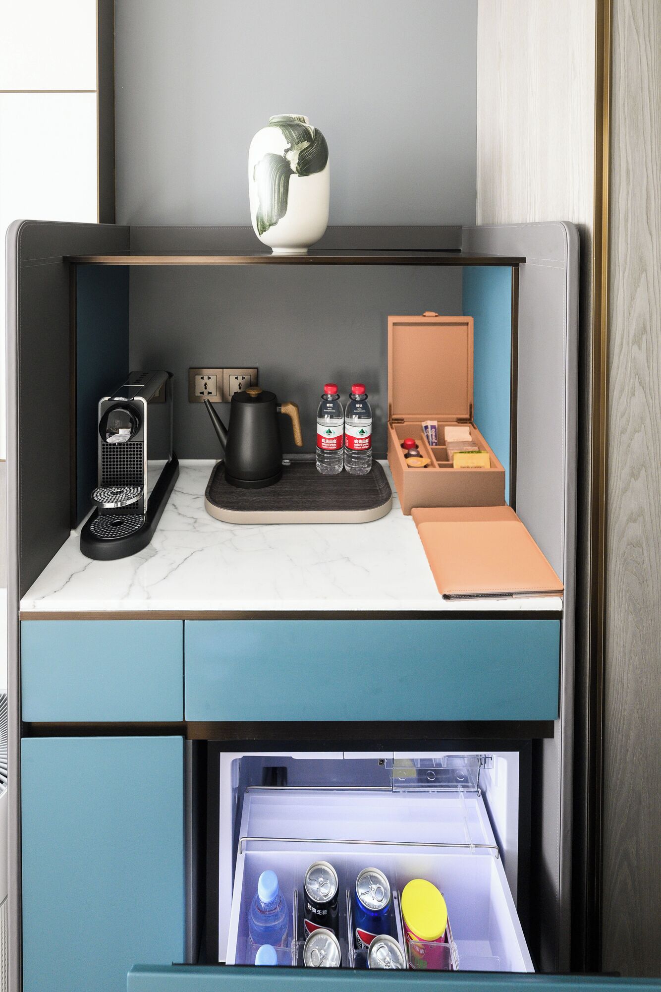 Una kitchenette moderna y compacta, equipada con cafetera, tetera y espacio para almacenar bebidas y snacks.