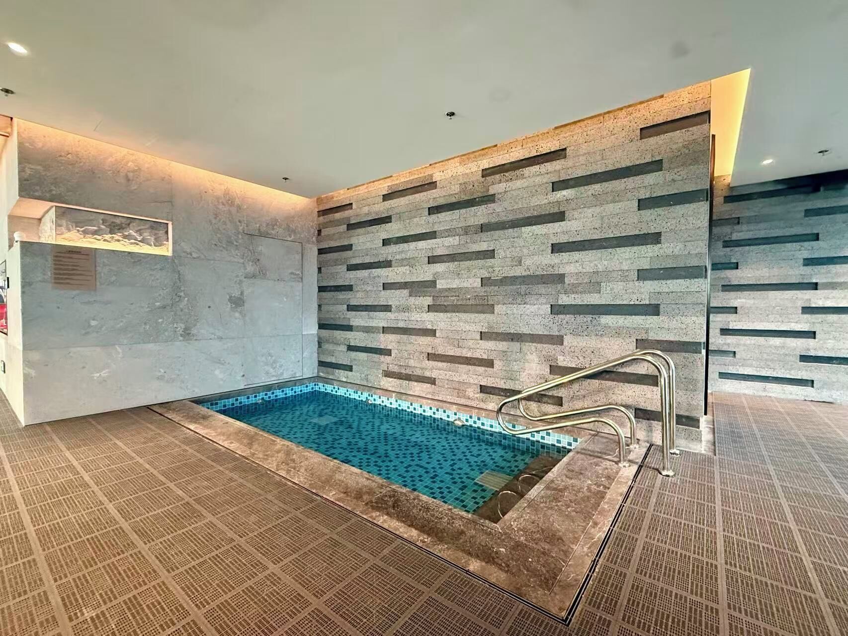 Ein moderner Innenpool mit gefliestem Boden und einer Wand mit geometrischem Muster.