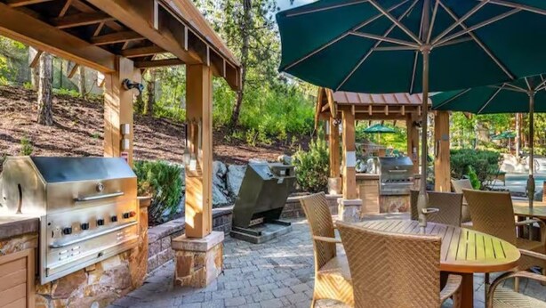 Un patio al aire libre con una parrilla, sillas de mimbre y una zona cubierta con una sombrilla.