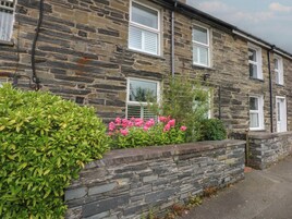 A stone building with multiple windows and a stone wall with greenery and flowers.