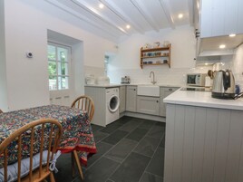 A compact kitchen with a washing machine, a sink, a microwave, and a kettle. There is a dining table with chairs and a window with a view.