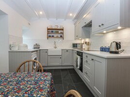 A compact kitchen with white cabinets, a microwave, a kettle, and a shelf with cups and a teapot.