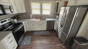 Une cuisine moderne avec des armoires blanches, des appareils en acier inoxydable, un plan de travail en bois et un dosseret décoré d’un motif en chevrons.