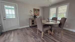 Un coin repas comprenant une table ronde, quatre chaises, un espace dédié au café et des œuvres d’art accrochées au mur.