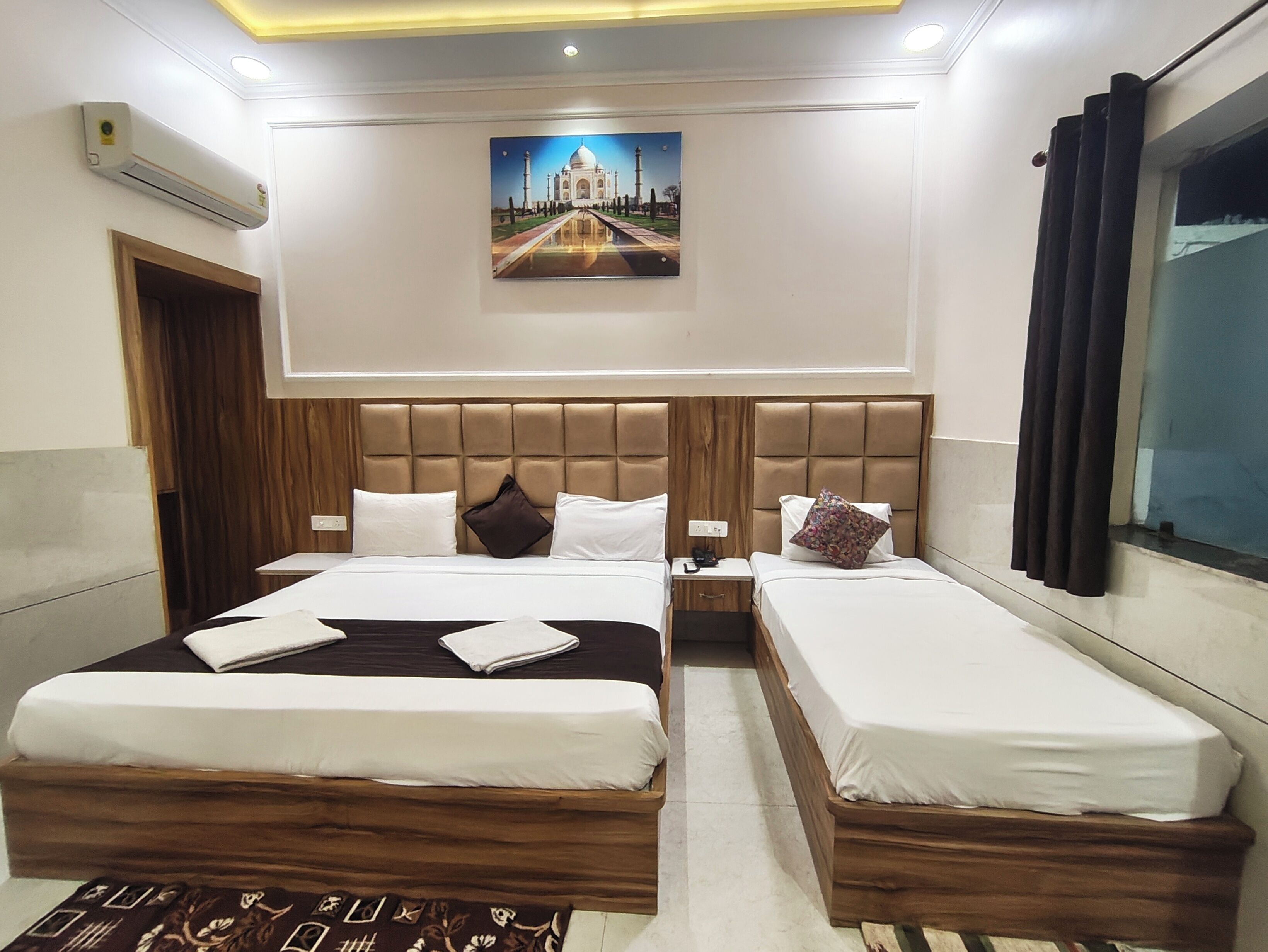 Habitación de hotel con dos camas, un cabecero de madera, un cuadro de un monumento famoso y un equipo de aire acondicionado.