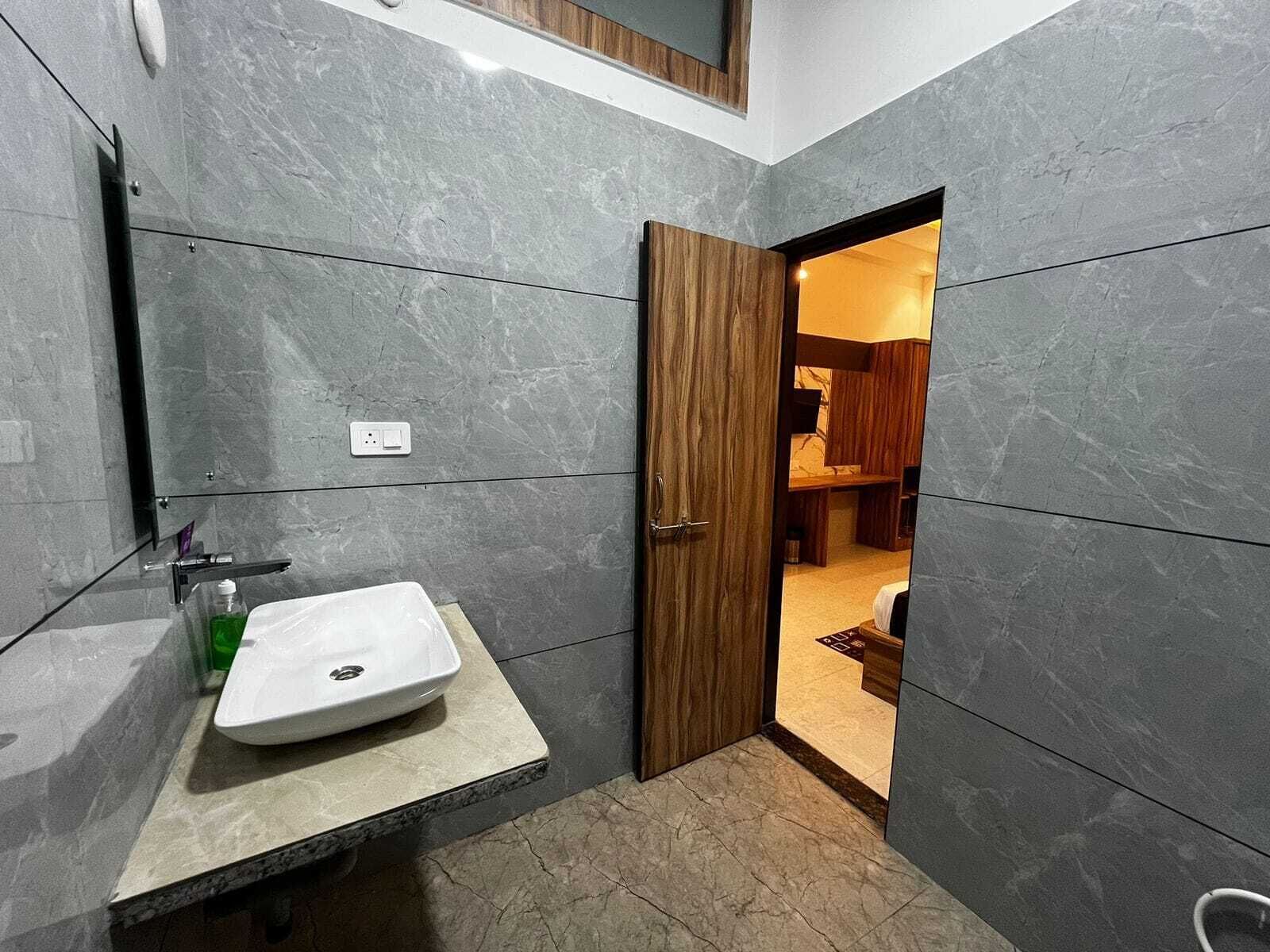 A modern bathroom with a white sink, wooden door, and grey tiled walls.