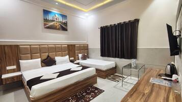 Una habitación de hotel moderna con dos camas, un cabecero de madera, un televisor de pantalla plana, un escritorio con un hervidor y un cuadro del Taj Mahal en la pared.