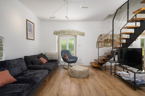 A modern living room with a black sofa, a rocking chair, a television, and a staircase. - Villa Veromi with heated pool in Istria (Orbani)