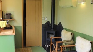 Una habitación acogedora con una cama, un aparador de madera, una pared verde, una estufa negra y una pequeña mesa con sillas.