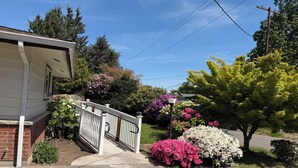 A residential house with a front porch, a white fence, and a variety of flowering bushes. - Charming villa with AC in Renton - perfect for large groups (Renton)