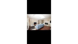 A modern living room with a skylight, a blue sofa, and a flat-screen TV. - Charming villa with AC in Renton - perfect for large groups (Renton)