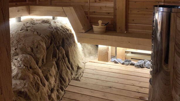 A wooden cabin with a stone wall, a metal container, and a wooden bench. - 3 bedroom chalet on the river, indoor sauna, close to the ski village (Mont-Tremblant)