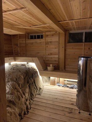 A wooden cabin with a stone wall, a metal container, and a wooden bench. - 3 bedroom chalet on the river, indoor sauna, close to the ski village (Mont-Tremblant)
