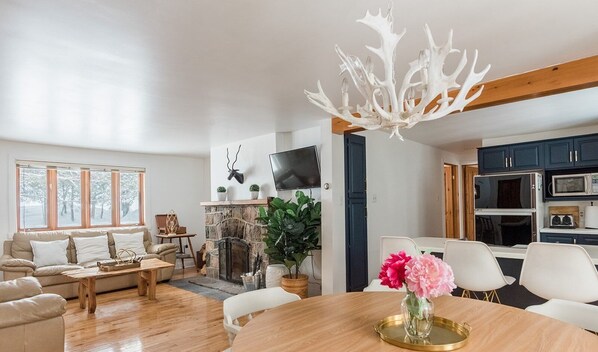 A modern living room with a fireplace, a dining area with a table and chairs, and a kitchen with cabinets and appliances. - 3 bedroom chalet on the river, indoor sauna, close to the ski village (Mont-Tremblant)