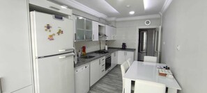 A compact kitchen with white cabinets, a refrigerator, a sink, and a dining area with a table and chairs.