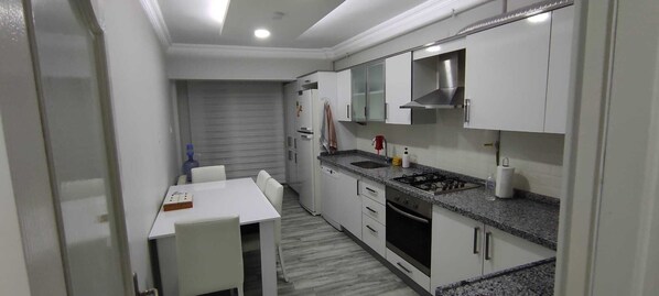A compact kitchen with white cabinets, a granite countertop, a gas stove, and a built-in oven.