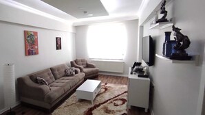 Un salon moderne avec un canapé beige, une table basse blanche et une bibliothèque remplie de livres.