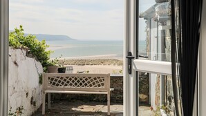Udsigt fra et værelse med en bænk og en dør, der fører ud til en balkon med udsigt over en strand og havet.