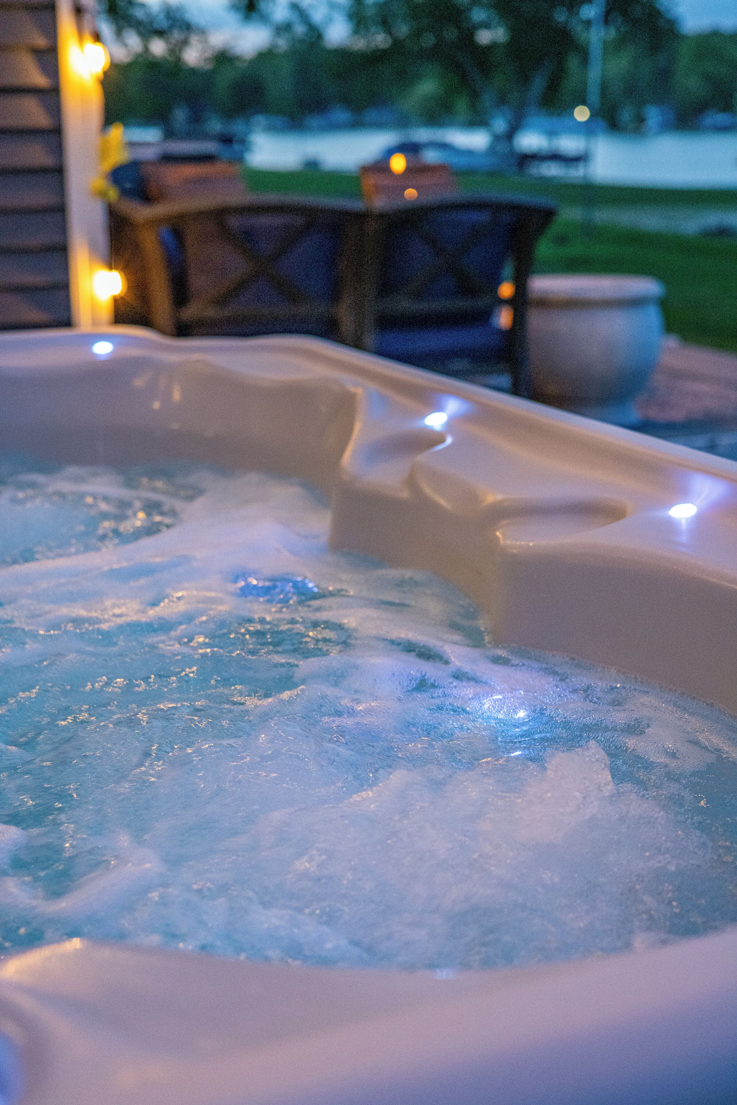 Un bain à remous avec une terrasse en bois et des meubles d’extérieur en arrière-plan.