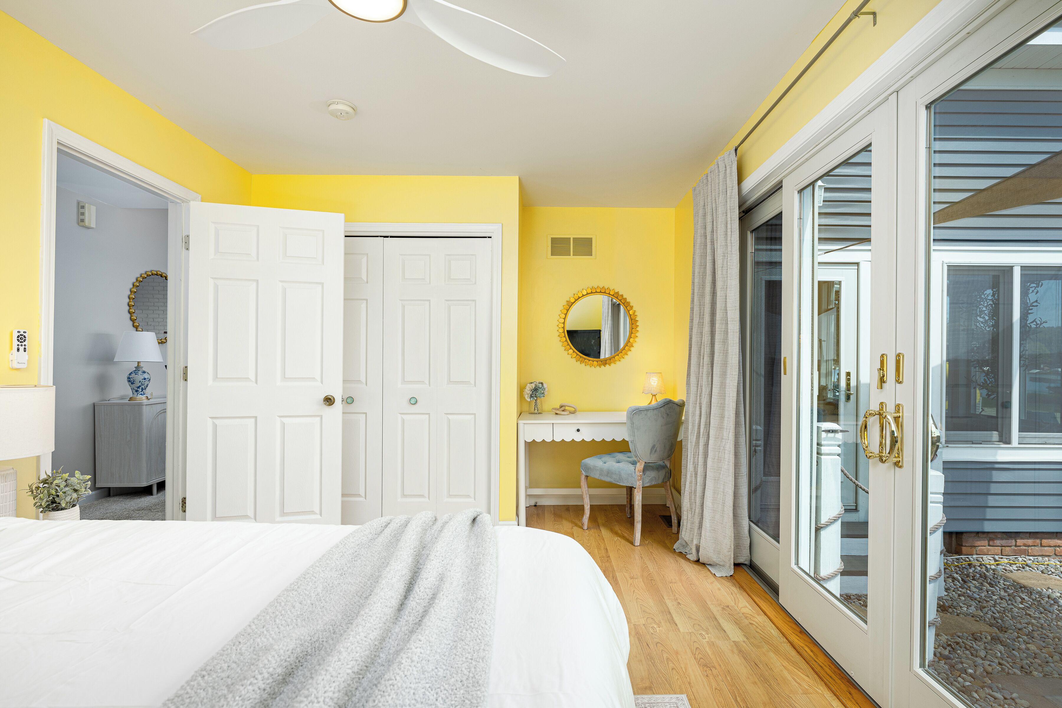 Une chambre comprenant un lit, un bureau, une chaise, un miroir et une porte-fenêtre coulissante donnant sur un espace extérieur.