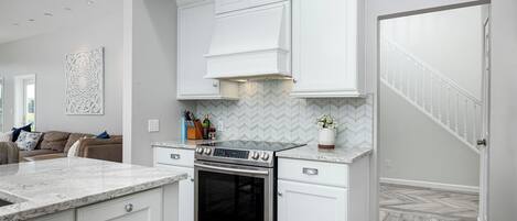 Una cocina moderna con armarios blancos, un horno de acero inoxidable y un salpicadero con diseño en espiga.